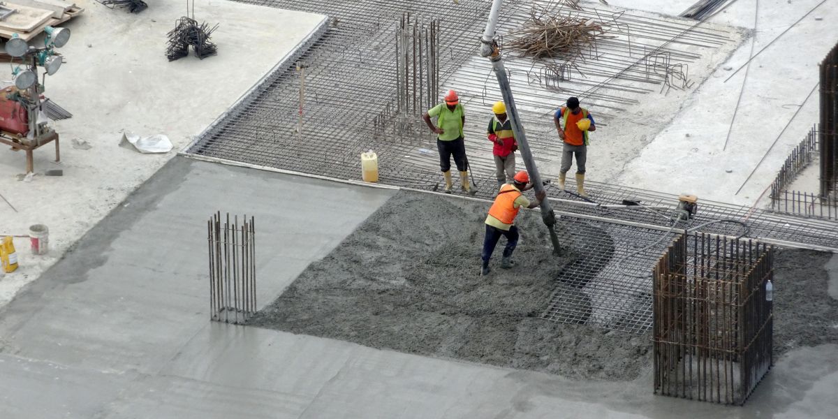 Operários da construção civil despejam concreto úmido usando uma mangueira de concreto em uma fôrma de laje no canteiro de obras