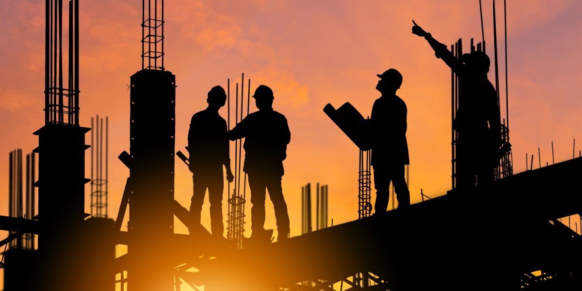 Silhueta de engenheiro e um operário em um canteiro de obras ao pôr do sol